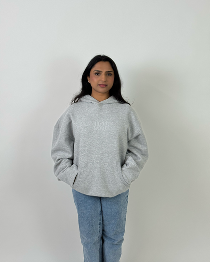 A woman wearing a light gray oversized sweatshirt and blue jeans, photographed against a plain light gray background.