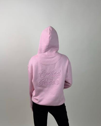 A person shown from the back wearing a light pink hoodie with 'Limited Edition' embroidered in matching pink script across the upper back, paired with black pants against a plain light gray studio background.
